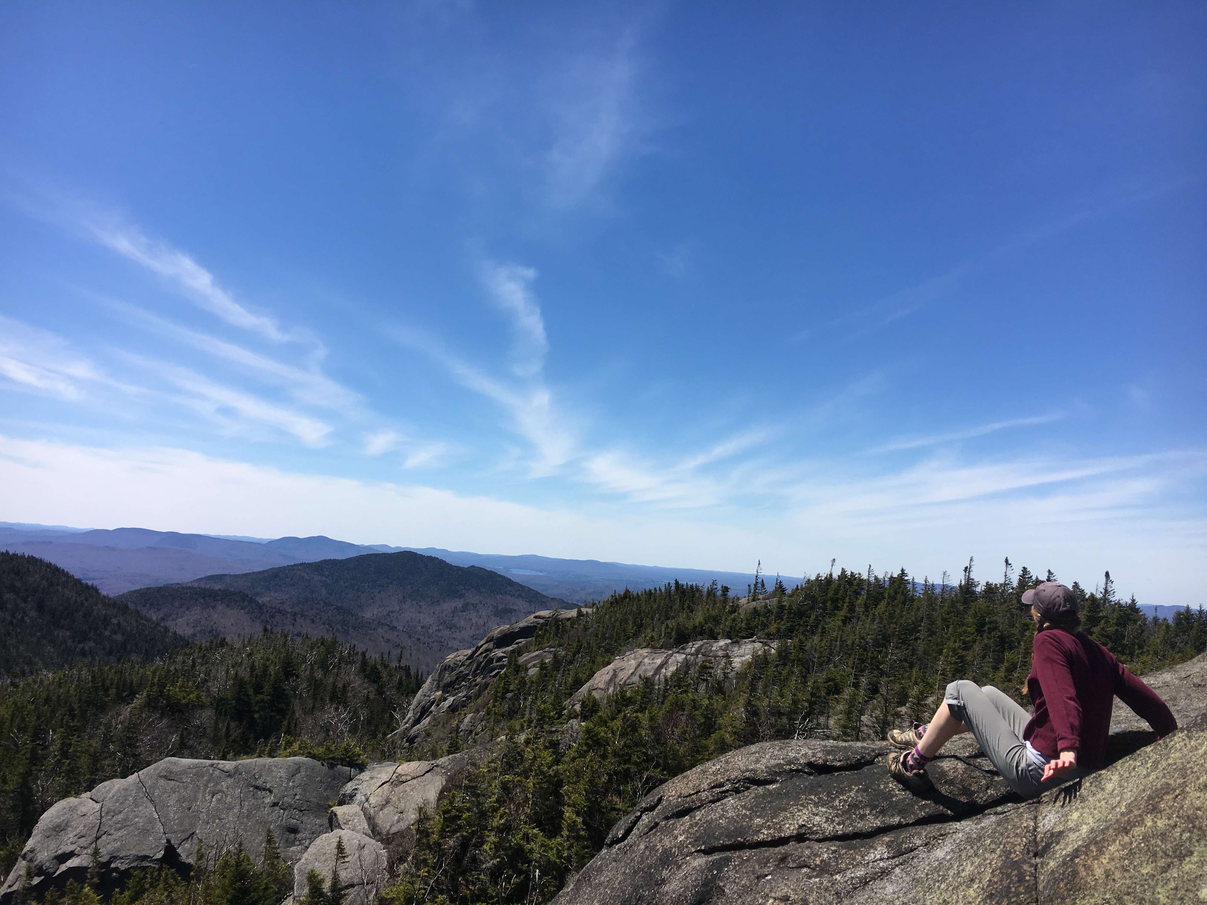 A hiker sits to the right on rocks on Ampersand Mountain in New York State's Adirondacks.