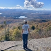 Liz stands on rock facing out over a view of trees in various shades of fall color change.