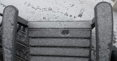 Slatted chair with snow on it shows imprint of birds feet and butt.